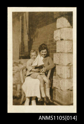 Betty Luke, Peter Luke's first wife, with a young boy sitting on her lap holding a model sailing boat