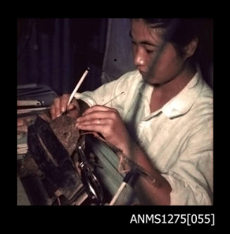 Colour negative of Yurie (or Yulie) George using dental tools to seed a pearl shell in a clamp