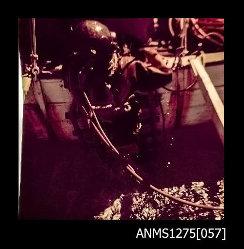 Colour negative of a person wearing a diving suit and helmet, in the water over the side of a boat