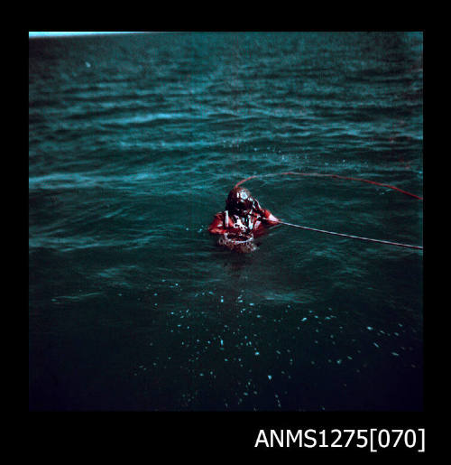 Colour negative of a man wearing a scuba diving outfit and helmet, in the water, with a rope attached