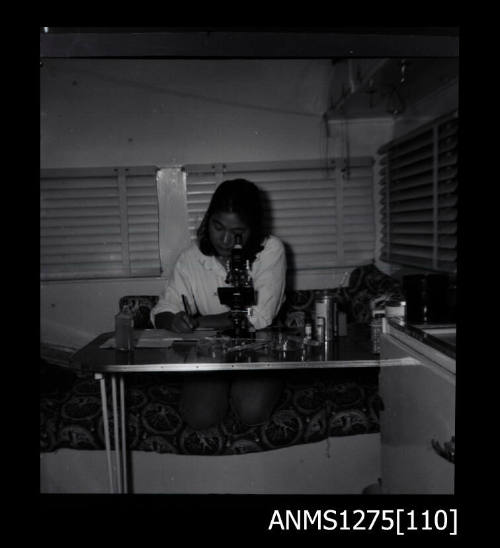 Yurie (or Yulie) George sitting at a desk looking through a microscope