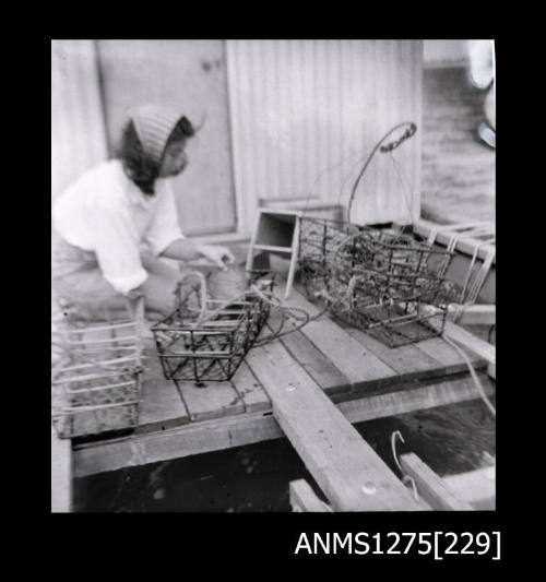 Yurie (or Yulie) George on a pearl raft, in front of a shed, surrounded by pearl cages