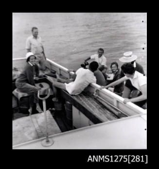 Several people in a boat, some of whom have moved into a smaller boat next to the larger boat