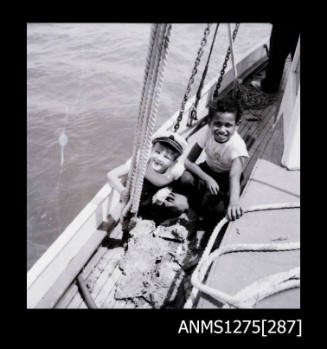 Two children on the edge of a pearl lugger, sitting behind a pile of pearl shells