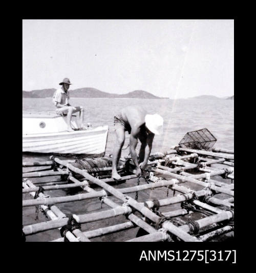 A man on  pearl raft pulling a rope out of the water, with a person sitting in a boat next to the raft