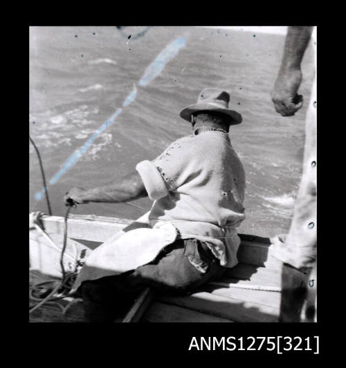 A man sitting on the edge of a boat, looking into the water and holding a rope