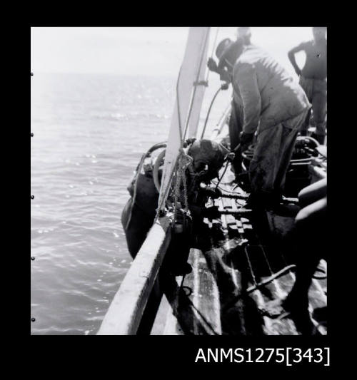 People standing on the side of a boat, pulling a person wearing diving gear and a large diving helmet into the boat