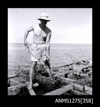 A man standing on a pearl raft, holding a pearl cage out of the water with rope