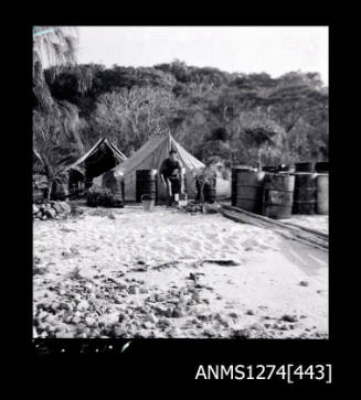 A person standing in front of two sheds and numerous metal, cylindrical containers, on Packe Island