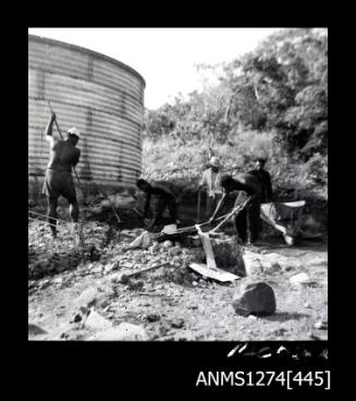 Five people digging in front of a large cylinder on Packe Island