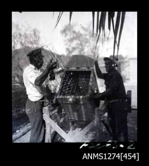 Two men putting pearl cages in a wooden box, used to clean the cages, on Packe Island