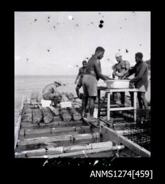 Several people on a pearl raft, surrounded by pearl shells, and washing [?] pearl shells in a large tub on a bench on Packe Island