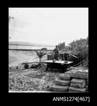 A man, standing on a beach, amongst pieces of equipment, on Packe Island