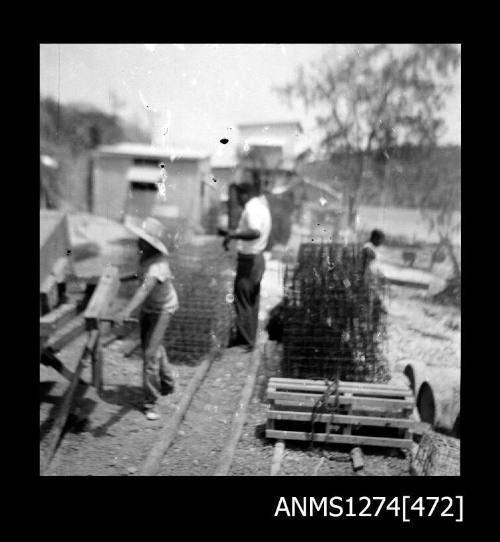 Two people standing next to pearl cages and other equipment, on Packe Island