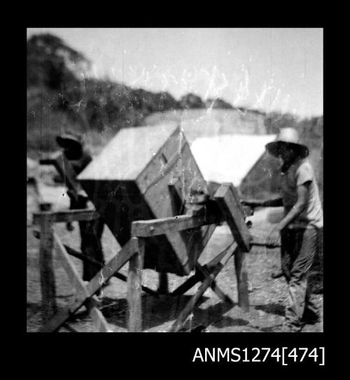 Two people standing near a piece of equipment, presumably a cage cleaning machine, on Packe Island