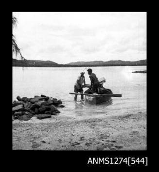 Two men and a boat, one standing in the boat, and the other standing in shallow water, on Packe Island