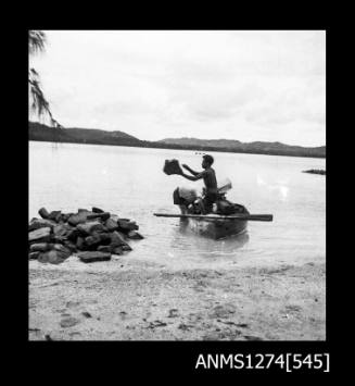 Two men and a boat, one standing in the boat, and the other standing in shallow water, on Packe Island