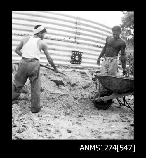 Two men, one shovellling, and one standing next to a wheelbarrow, on Packe Island