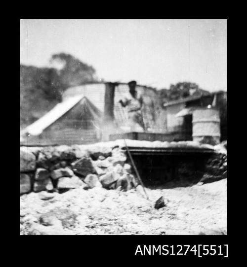 A man standing on a rock wall, next to metal cylinders, and in front of a tent, on Packe Island