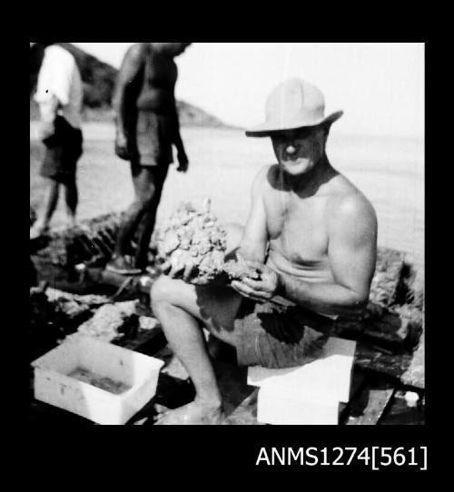 Several men working on a pearl raft on Packe Island, with the sitting man holding a pearl shell