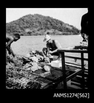 Several men working on a pearl raft on Packe Island, amongst pearl cages and pearl shells