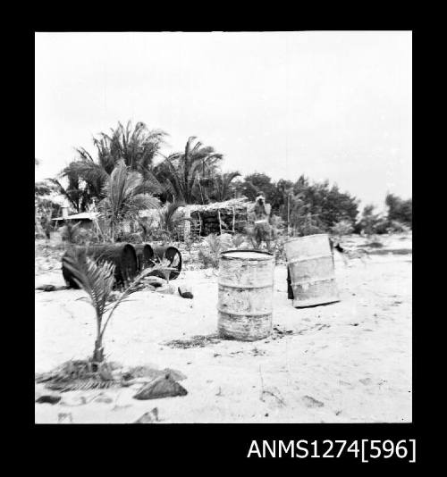 Beach, with a shed, palm trees and metal containers, on Packe Island