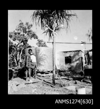 Two men standing next to a shed and large metal cylinder, on Packe Island