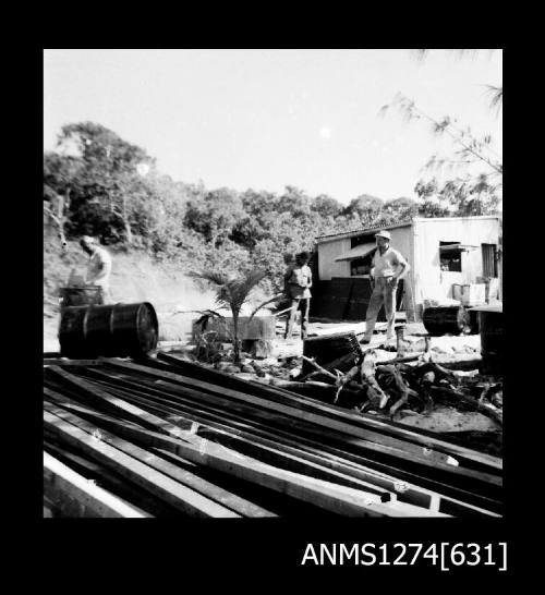 A man, standing under a shade cloth surrounded by equipment, on Packe Island