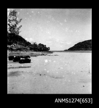 Shoreline on Packe Island, with three metal cylinders floating in the water