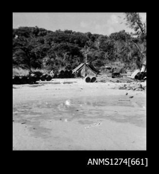 Shoreline on Packe Island, with a tent, planks of wood, and metal cylinders