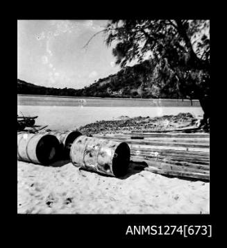 Metal cylindrical containers and wood planks which are lying on the shoreline on Packe Island