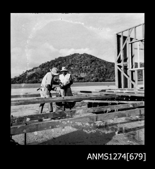 Two men building a lab, on the water, on Packe Island