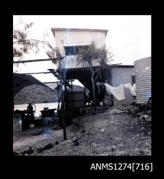 A two-storey house on Packe Island, next to a large metal cylinder, and with wshing hanging out the front