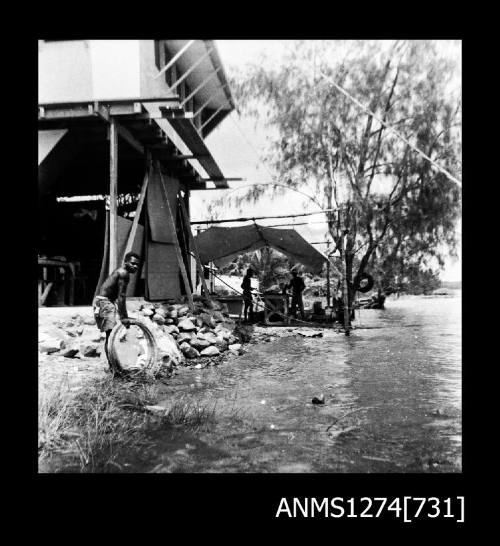 A two story house on Packe Island, with three people working with equipment under a shade cover