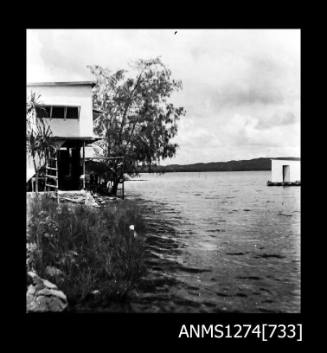 Two black-and-white negatives, joined together, of a two storey house on Packe Island, with a pearl raft in the water near the house