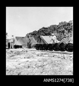 Seven metal drums in a row, in front of two tents on Packe Island