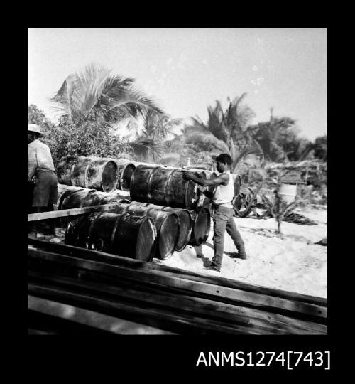 Two people stacking metal drums on top of each other, on Packe Island