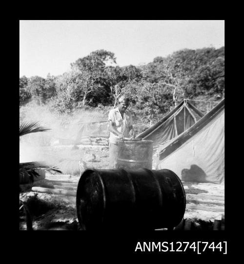 A man standing in front of a metal drum, beside a tent, on Packe Island