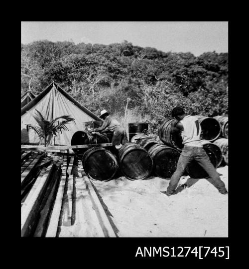 Two men moving and stacking metal drums on Packe Island