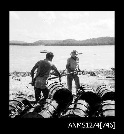 Two men holding a wooden beam to attached the drums, on Packe Island