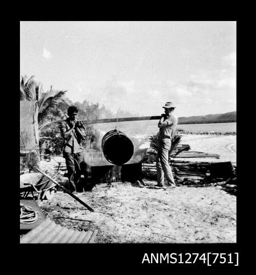 Two men carrying a metal drum with a wooden beam, on Packe Island