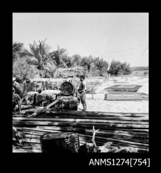 A man stacking metal drums, next to a large pile of wood, on Packe Island