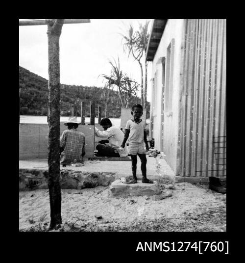 A young boy standing beside two men working on large, rectangular shaped pieces of equipment on Packe Island