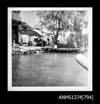 Photograph of sheds, a shade cloth and equipment on the shoreline on Packe Island