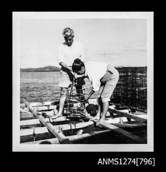 Yurie (or Yulie) George with a man on a pearl raft, pulling a pearl cage out of the water, on Packe Island