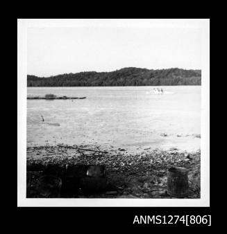 Photograph, possibly of a pearl raft and boat, in the water on Packe Island, with metal containers visible on the shoreline