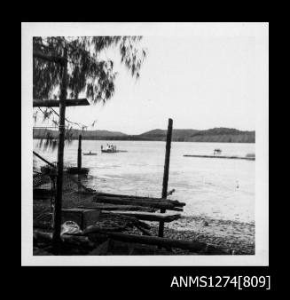 Wood, wire and other equipment on a beach on Packe Island, with people in boats in the water, near a pearl raft