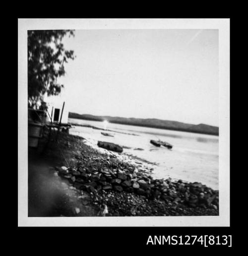 Photograph of shoreline, and a pearl raft in the water, on Packe Island