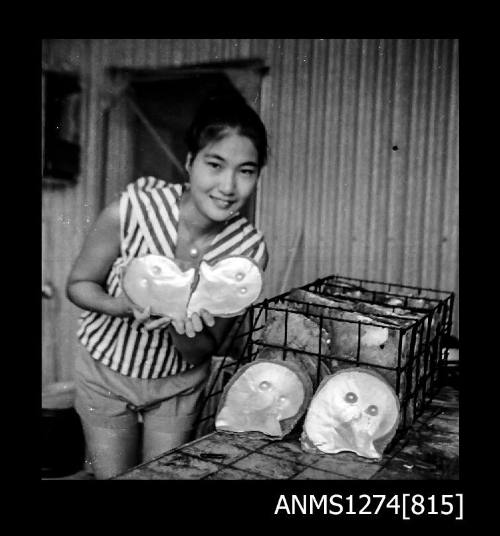 Yurie (or Yulie) George holding two pearl shells, next to a pearl cage with two pearl shells sitting at the front, on Packe Island