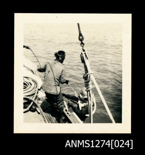 A person over the side of a boat, with a scuba diving helmet on, being lowered into the water with the assistance of a male, with a rope, on Packe Island